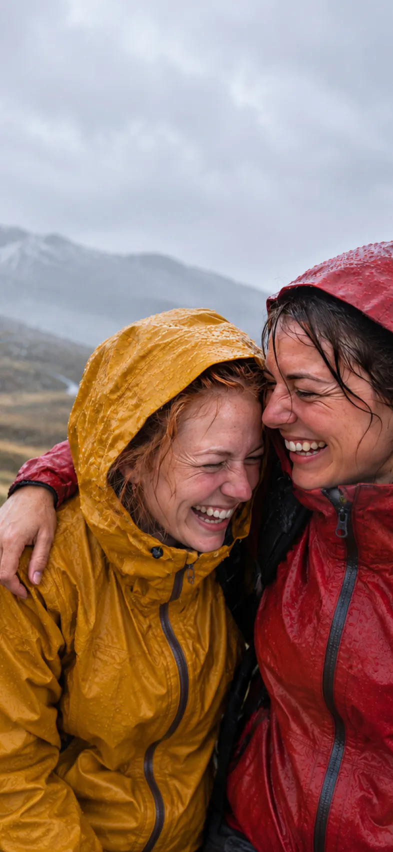 Two friends in rain jackets laughing together on a wet hillside